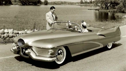 Vintage Buick LeSabre convertible parked by a lakeside, with a man and woman dressed in mid-20th century attire, featured in an HD PC desktop wallpaper background.
