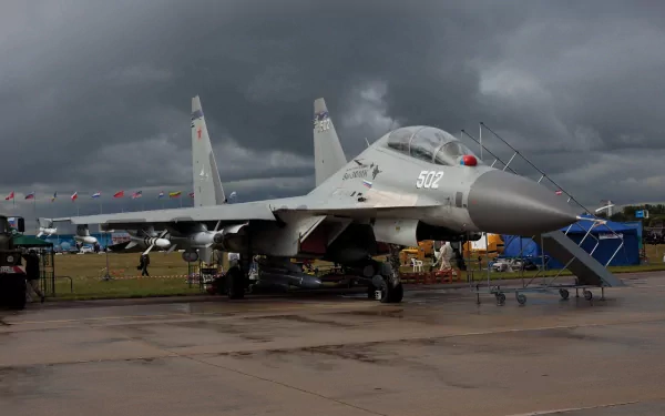 HD desktop wallpaper featuring a Sukhoi Su-30 military aircraft on a wet tarmac with a cloudy sky in the background.