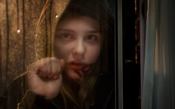 HD desktop wallpaper of Chloë Grace Moretz in the movie Let Me In, depicting her looking through a window with a solemn expression and a hand pressed against the glass.