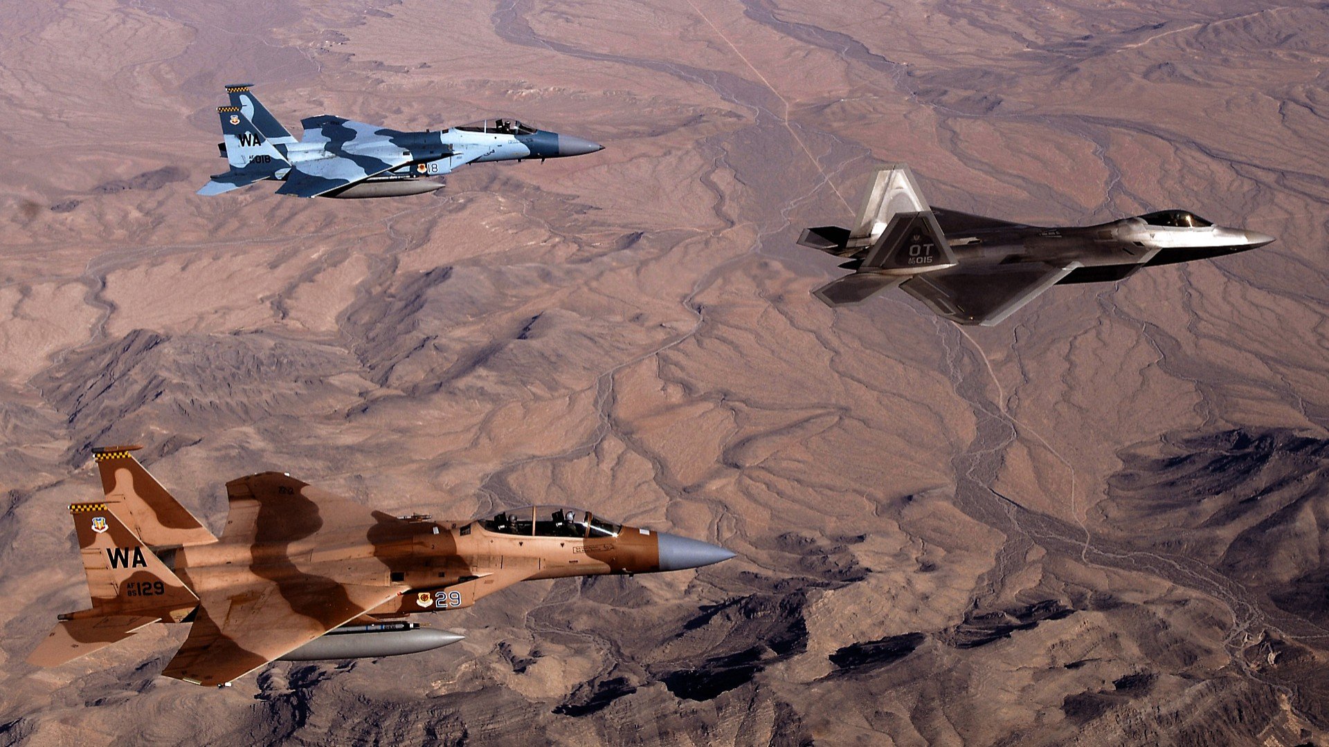 Aerial HD wallpaper showing a McDonnell Douglas F-15 Eagle, Lockheed Martin F-22 Raptor, and a third military jet fighter flying over a desert landscape.