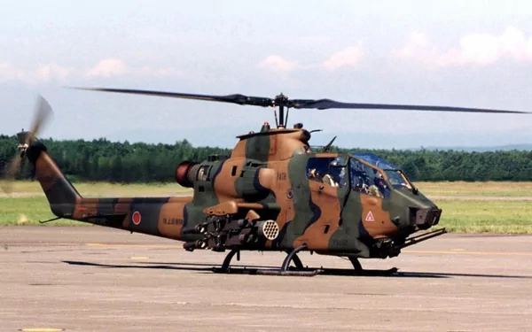 HD desktop wallpaper featuring a military Bell AH-1 SuperCobra helicopter on a runway with a forest backdrop.