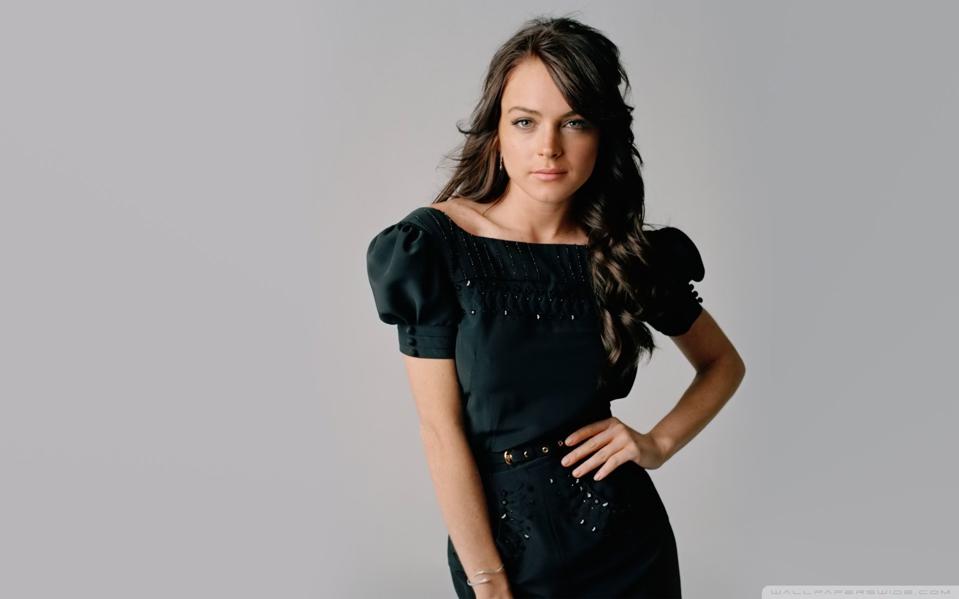 HD desktop wallpaper featuring celebrity Lindsay Lohan posing confidently against a light gray background, wearing a stylish black dress with puffed sleeves.