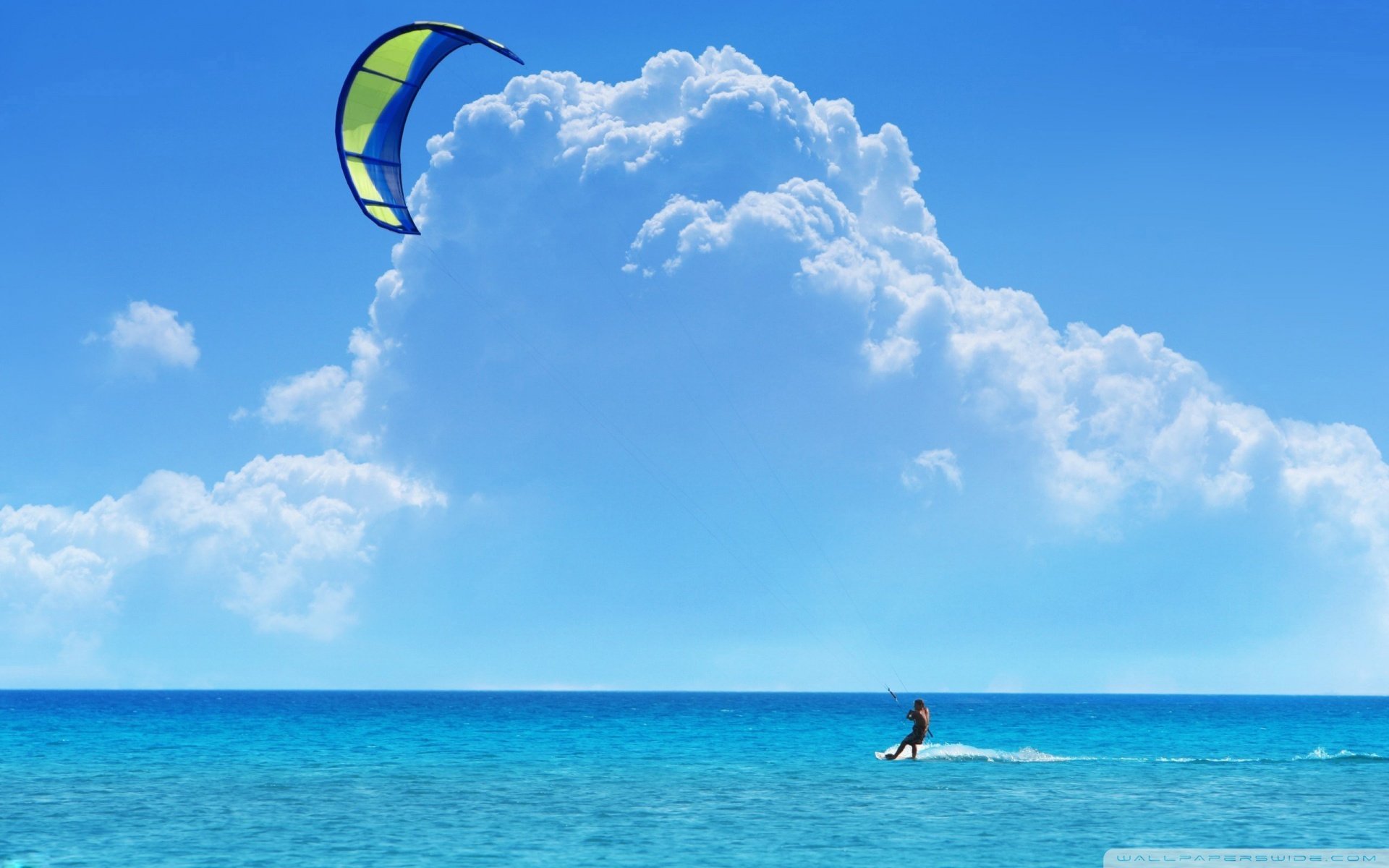 HD PC desktop wallpaper and background: windsurfing sports scene — a lone windsurfer skimming turquoise sea beneath a bright blue sky and towering white clouds.