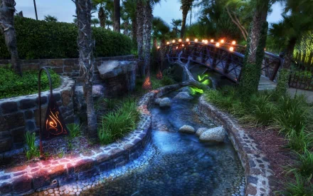 A serene HDR photograph of a winding stream under a bridge, illuminated by soft lights, surrounded by lush greenery and palm trees, creating a tranquil landscape scene.