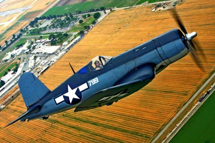 HD desktop wallpaper showing a vintage military aircraft flying over farmland with clear skies and detailed landscape below.
