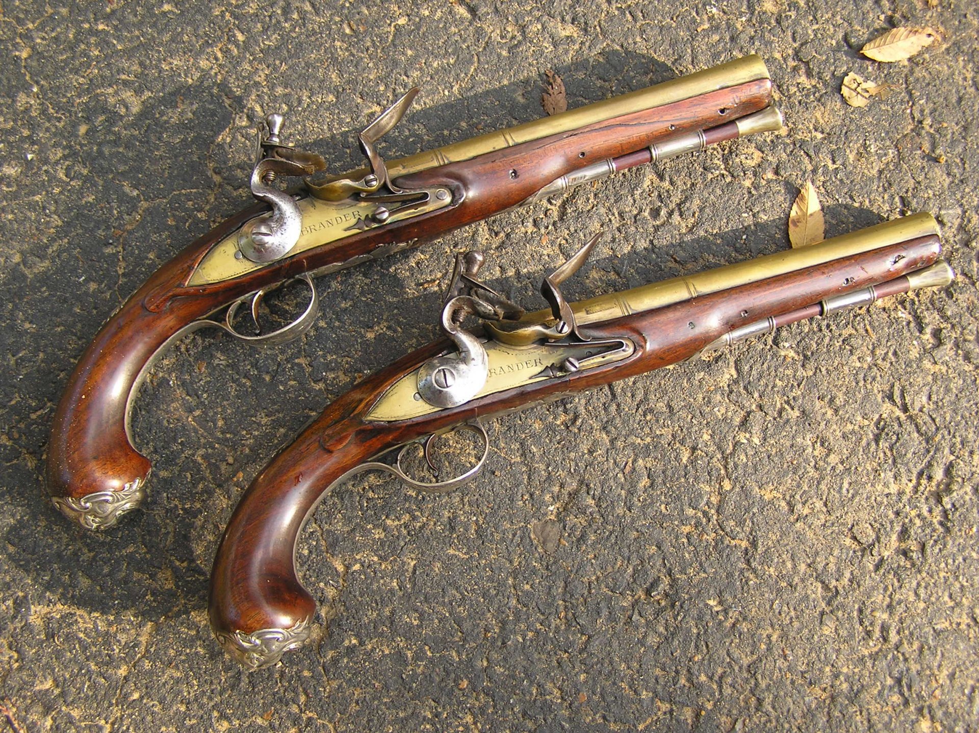 HD desktop wallpaper featuring two man-made flintlock pistols with wooden stocks and metal details resting on a textured stone surface.