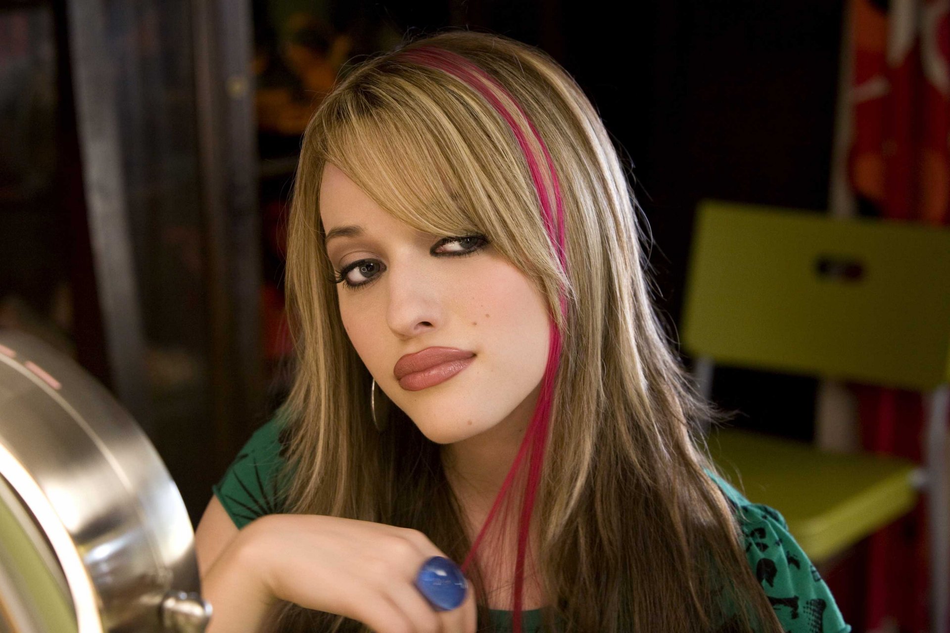HD PC desktop wallpaper featuring celebrity Kat Dennings with blonde hair and a pink streak, wearing a green top and gazing thoughtfully.