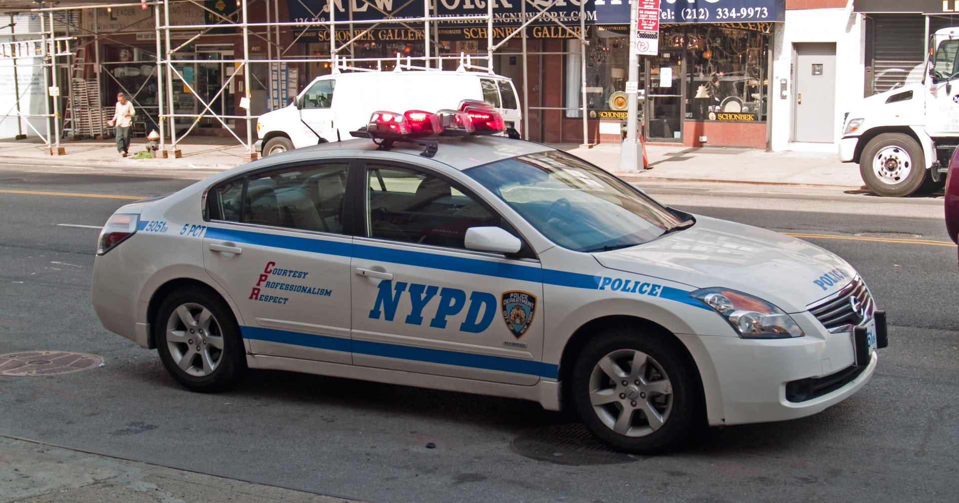 NYPD police patrol sedan with roof lights parked on a city street, presented as a 2K Quad HD PC desktop wallpaper and background.