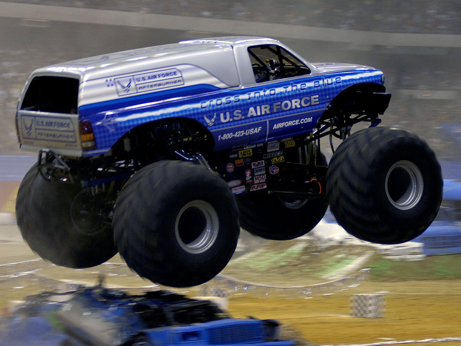 HD desktop wallpaper of a U.S. Air Force-themed monster truck in mid-air during a jump at an indoor event.