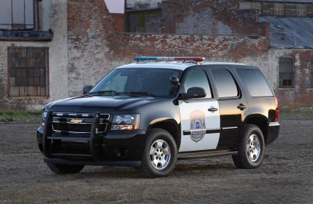 2K Quad HD PC desktop background showing a black-and-white police SUV parked on gravel before a weathered brick industrial building.