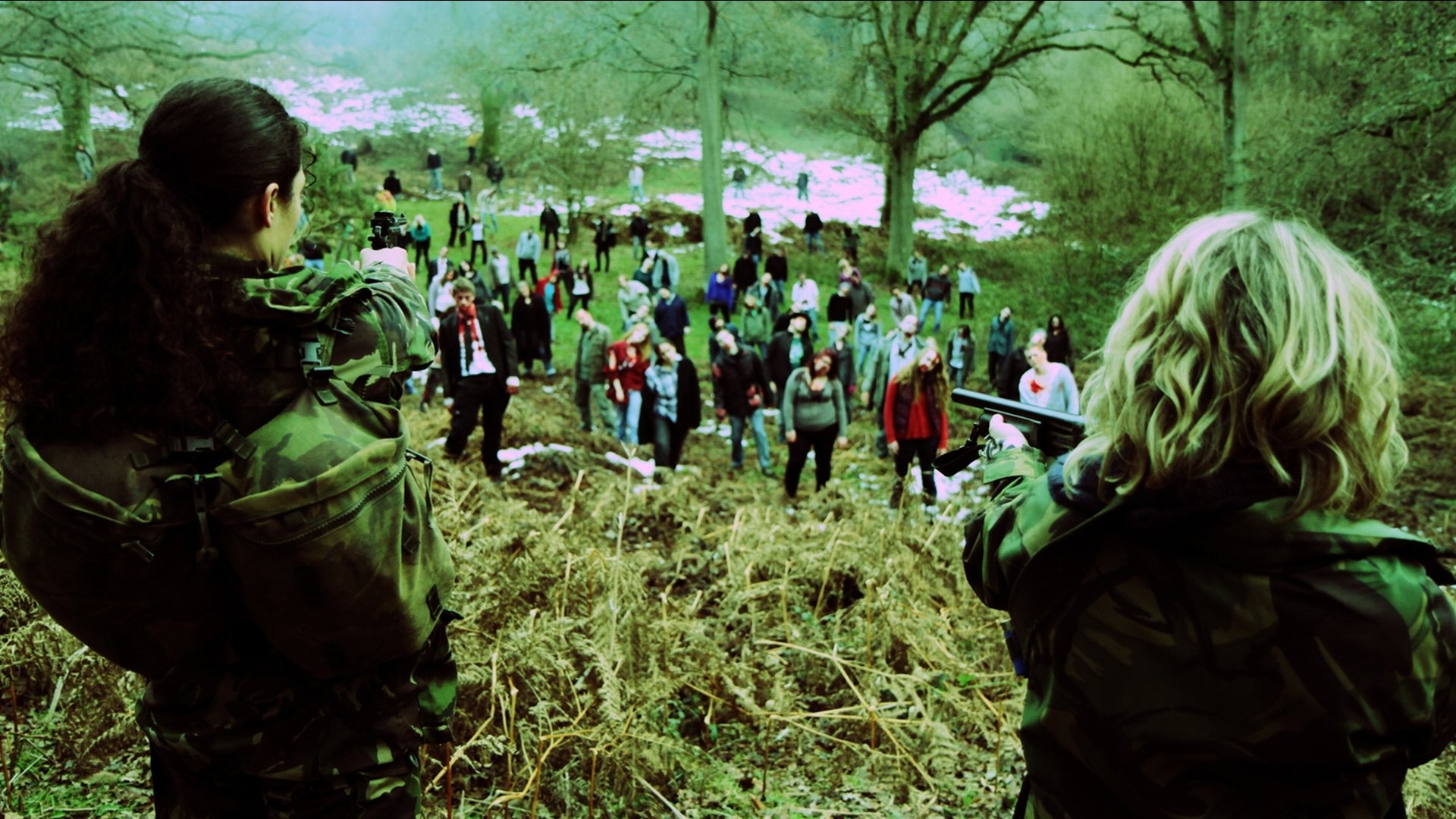 HD PC desktop wallpaper from the movie Zombie Diaries 2: two armed survivors aim at a descending horde of zombies across a grassy hillside under bare trees.