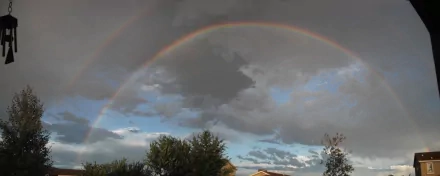 2K Quad HD PC desktop wallpaper of Arizona nature: vibrant rainbow arching across a stormy sky above trees and rooftop silhouettes.