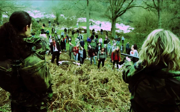 HD PC desktop wallpaper from the movie Zombie Diaries 2: two armed survivors aim at a descending horde of zombies across a grassy hillside under bare trees.