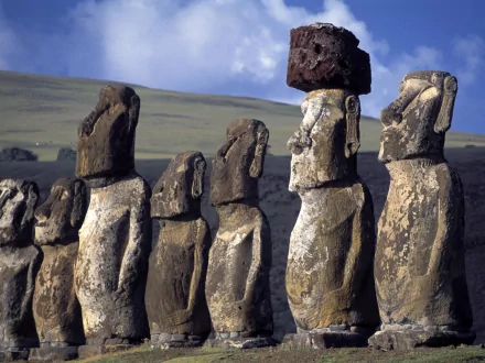 A striking HD desktop wallpaper featuring iconic moai statues, showcasing their unique man-made forms against a scenic backdrop of rolling hills and a blue sky.