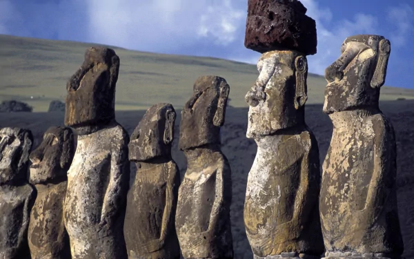 A striking HD desktop wallpaper featuring iconic moai statues, showcasing their unique man-made forms against a scenic backdrop of rolling hills and a blue sky.