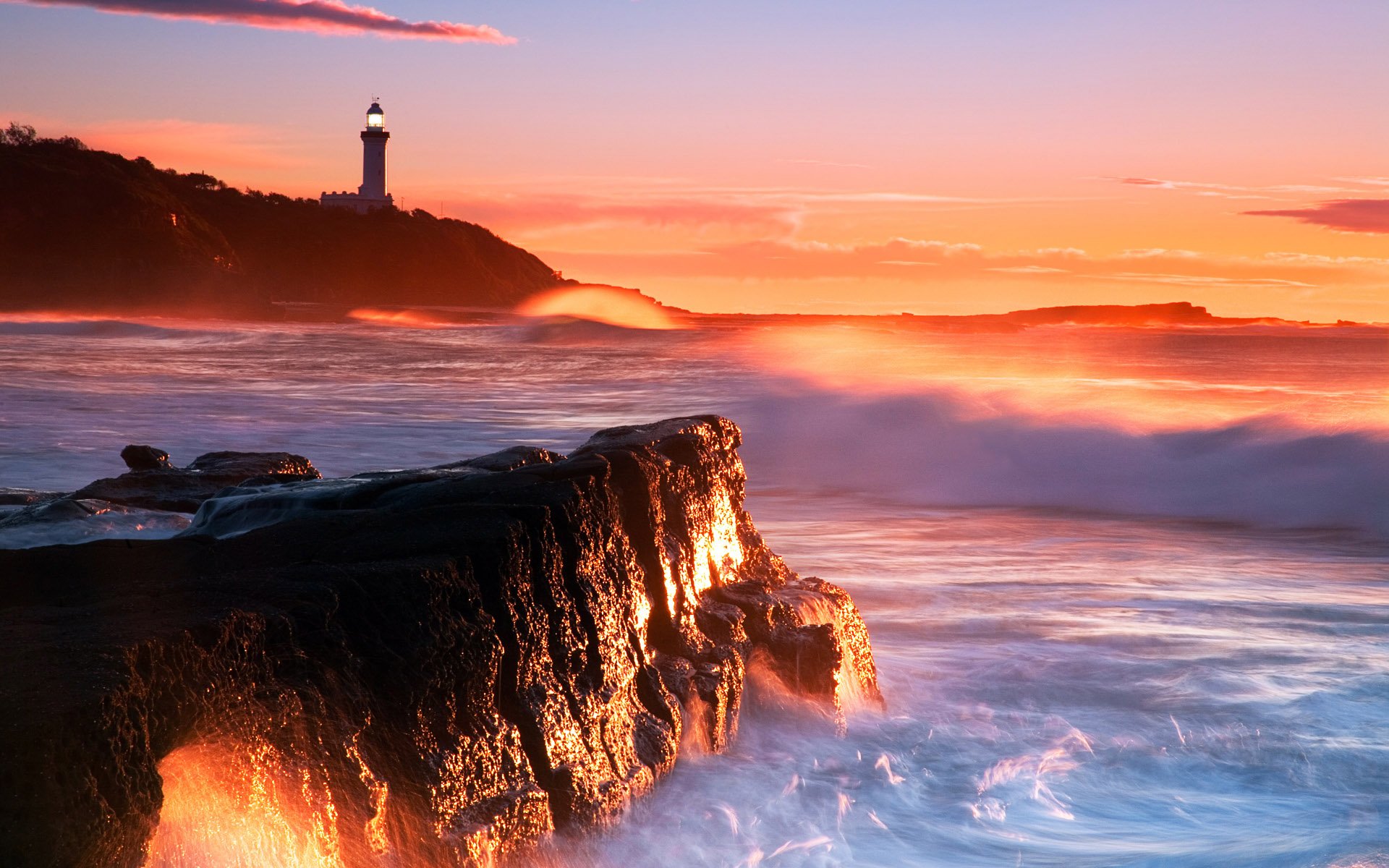 A stunning sunset illuminates the coastline, with waves crashing against rocky shores and a lighthouse standing tall against the orange sky, creating a captivating ocean scene.