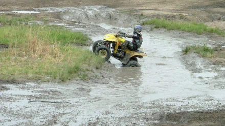 HD desktop wallpaper featuring a Suzuki ATV and rider navigating through a muddy off-road terrain.