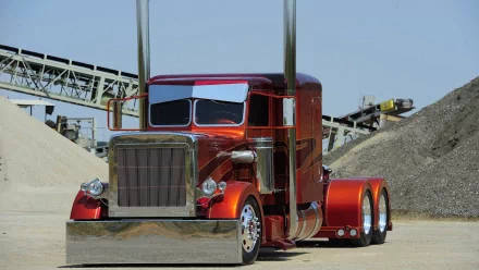 A vibrant red truck with a shiny metallic finish and tall exhaust stacks parked on a construction site with machinery in the background. HD desktop wallpaper featuring a striking vehicle.