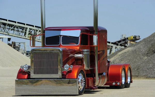 A vibrant red truck with a shiny metallic finish and tall exhaust stacks parked on a construction site with machinery in the background. HD desktop wallpaper featuring a striking vehicle.