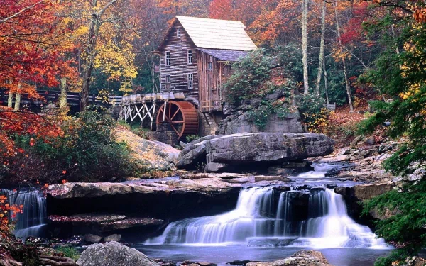 HD desktop wallpaper of a man-made watermill nestled among vibrant autumn trees with a cascading waterfall in the foreground.