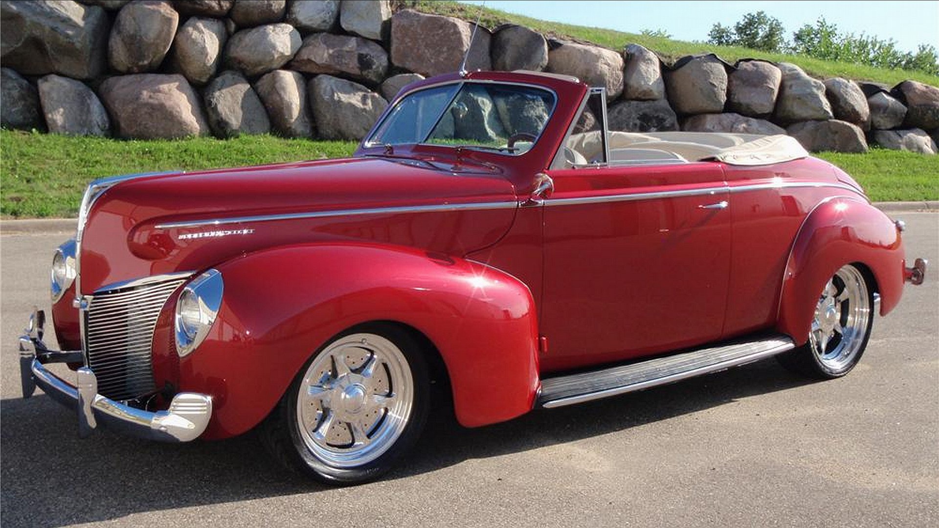 Glossy red vintage Mercury convertible parked on a road before a stone wall, presented as a 4K Ultra HD PC desktop wallpaper/background.