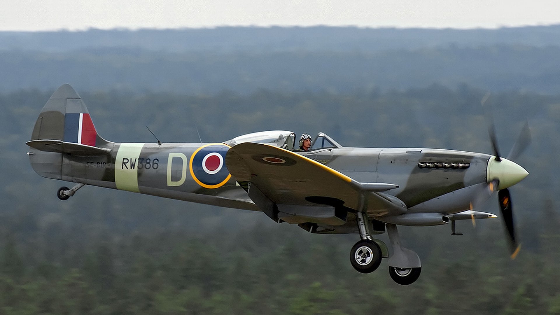 4K Ultra HD desktop wallpaper featuring a vintage military aircraft in mid-flight against a blurred natural landscape background.