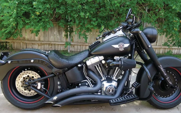4K Ultra HD PC desktop wallpaper of a black cruiser motorcycle (vehicle) with V-twin engine, matte finish and red-striped tires parked by a wooden fence and leafy hedge.