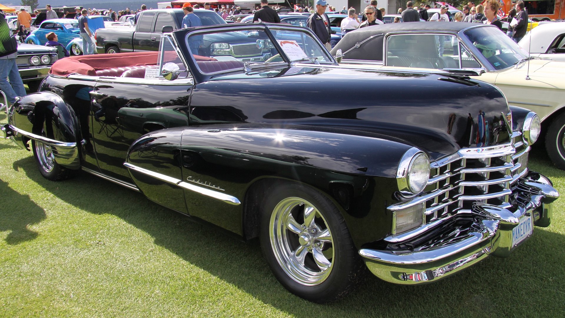 HD PC desktop wallpaper featuring a sleek black vintage convertible car displayed at an outdoor car show with other classic vehicles in the background.