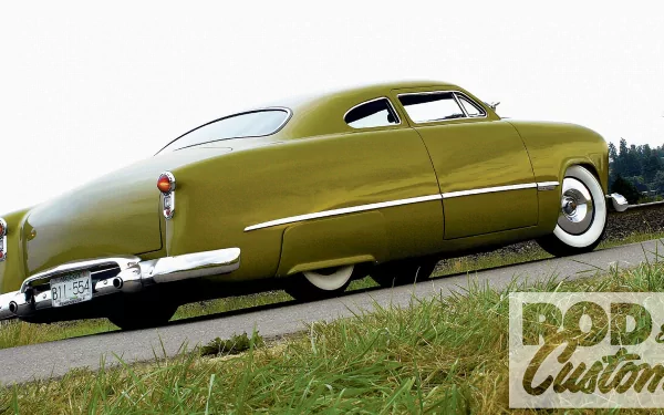 Lowrider Ford vehicle in olive green with whitewall tires, photographed low-angle on the roadside; HD PC desktop wallpaper and background.