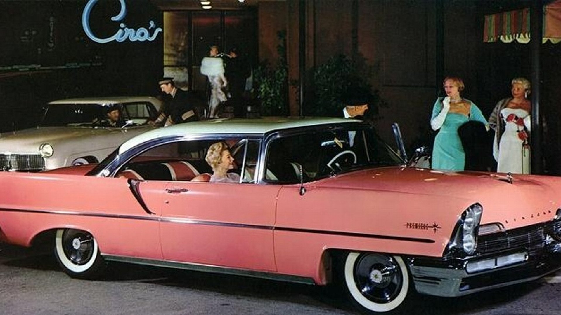 HD PC desktop wallpaper of a vintage pink Lincoln parked outside a neon-lit restaurant at night, with well-dressed people standing and conversing nearby.