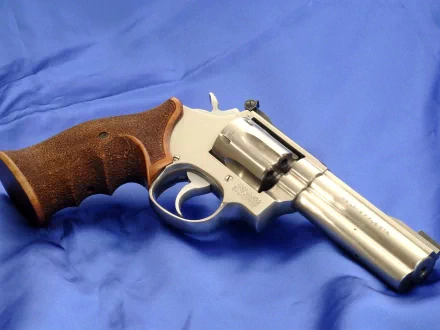 HD desktop wallpaper featuring a close-up of a man-made silver revolver with a wooden grip resting on a blue fabric background.