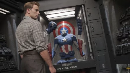 A high-definition wallpaper featuring Chris Evans as Captain America, standing before a display case with his iconic suit and shield from the Avengers movie series.