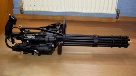 HD desktop wallpaper featuring a detailed close-up of a man-made M134 Minigun displayed indoors on a wooden floor.