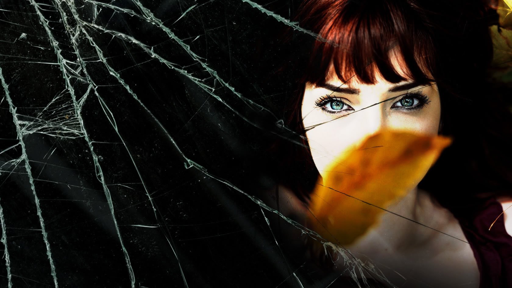 HD PC desktop wallpaper: close-up of a red‑haired model/celebrity with striking blue eyes, an orange leaf partially covering her face set against a cracked‑glass texture.