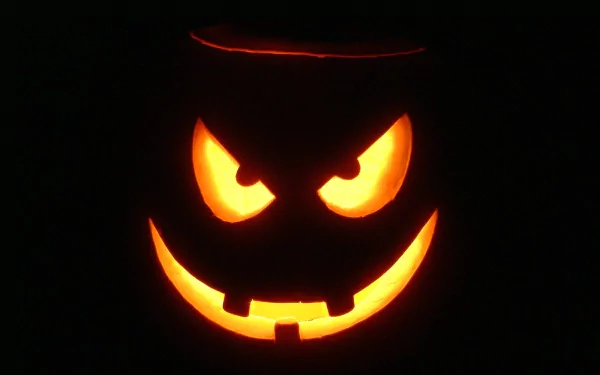 A glowing carved pumpkin with a menacing face illuminates the darkness, capturing the spooky essence of Halloween in this HD desktop wallpaper and background.