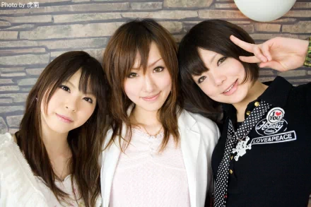 Three Asian women posing together, standing in front of a brick wall. One has a peace sign up, exuding a friendly and sensual vibe. This vibrant HD desktop wallpaper captures their charming expressions.
