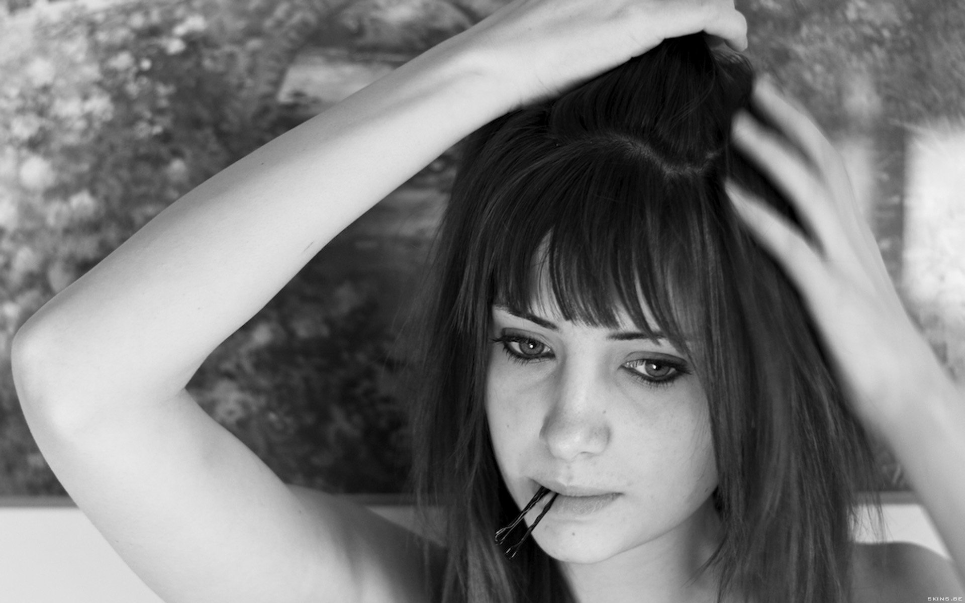Black-and-white HD desktop wallpaper: close-up portrait of a pensive woman with bangs, hand in her hair and a toothpick between her lips against a softly textured background.