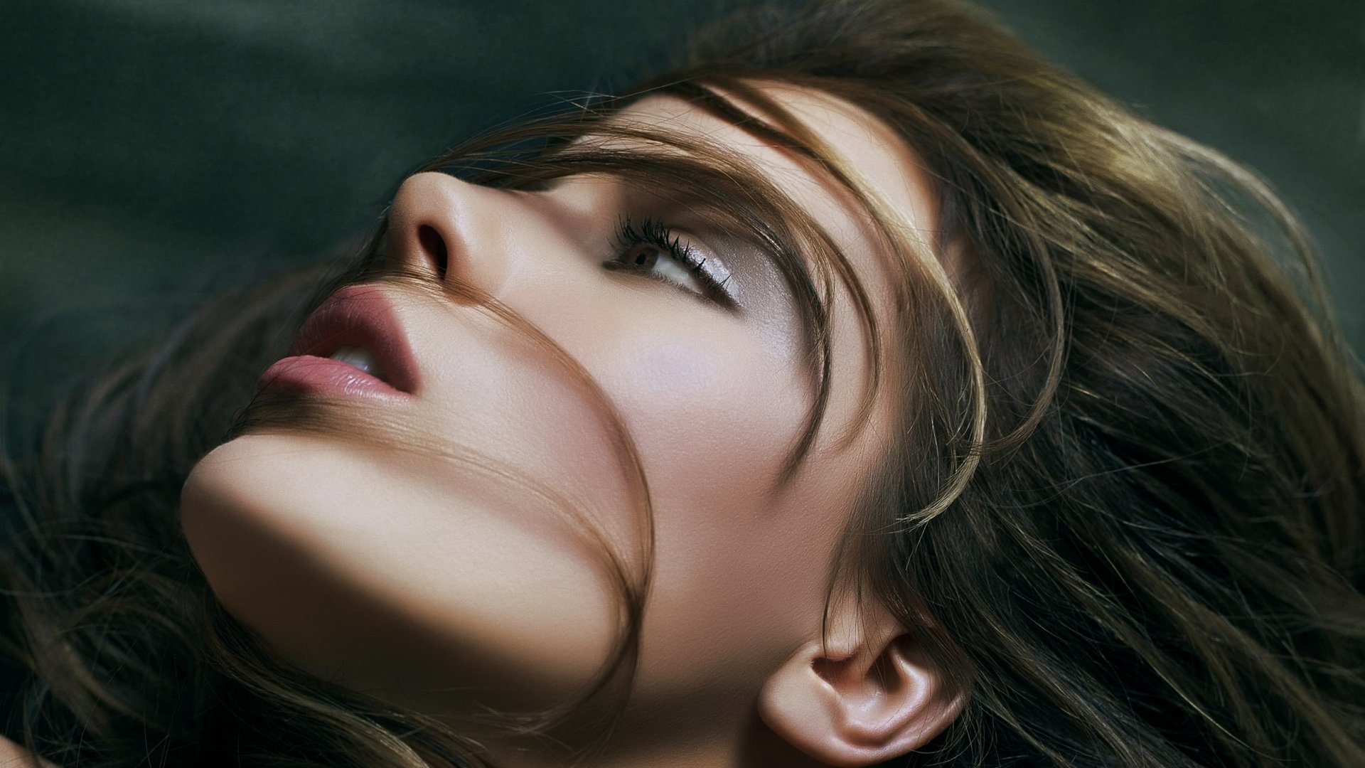 Close-up HD desktop wallpaper of a woman in profile with windblown hair, smoky eye makeup and soft, cinematic lighting, a glamour portrait with a serene, upward gaze.