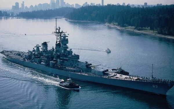 HD desktop wallpaper featuring the military battleship USS Missouri (BB-63) sailing through a calm waterway with a city skyline in the background.