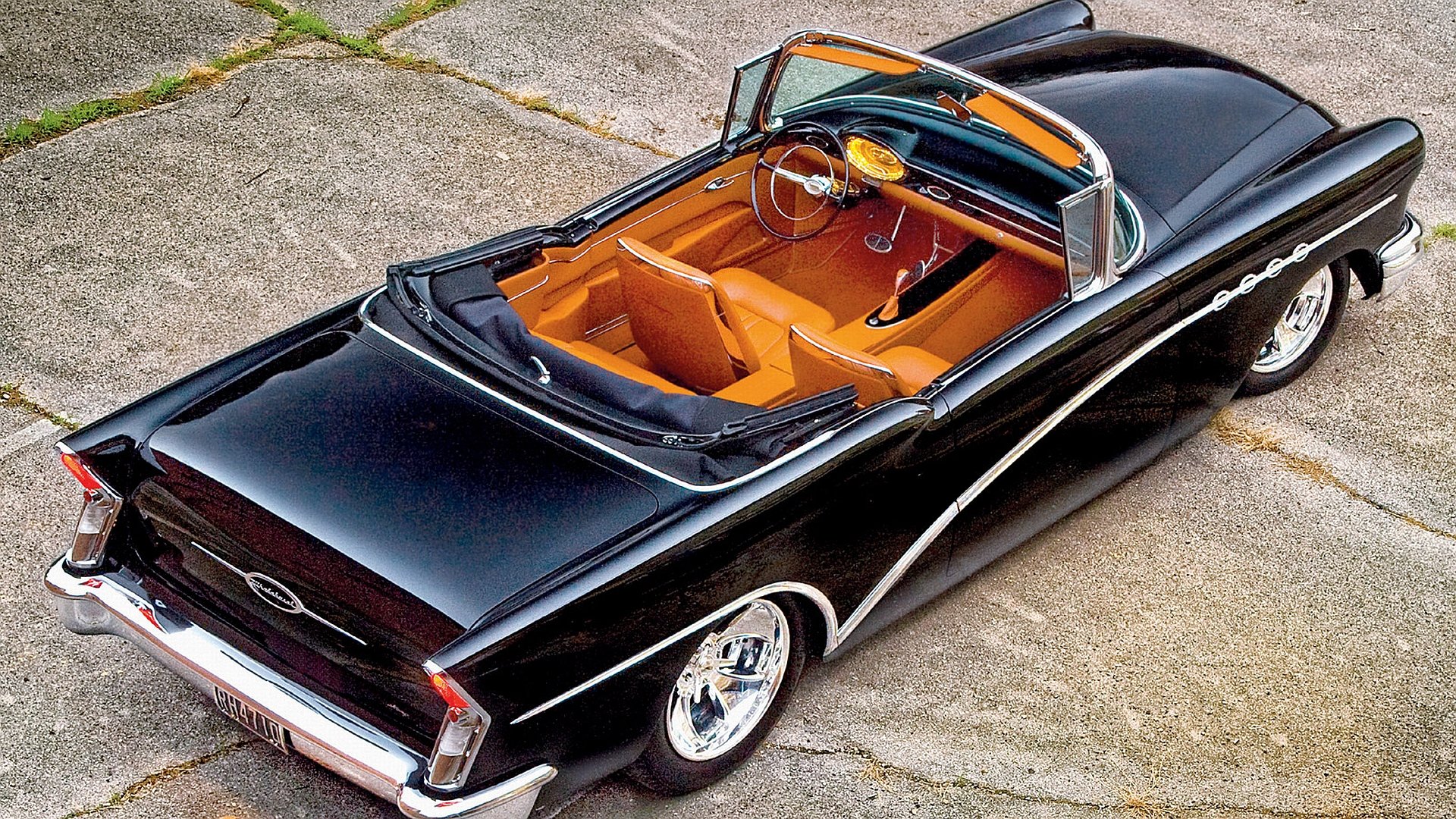 HD PC desktop wallpaper and background: glossy black Buick convertible vehicle with tan leather interior and chrome trim, top down on cracked concrete.
