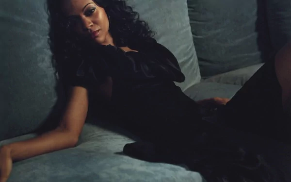 HD desktop wallpaper featuring celebrity Zoe Saldana reclining on a plush sofa in a dark, elegant outfit with soft lighting.