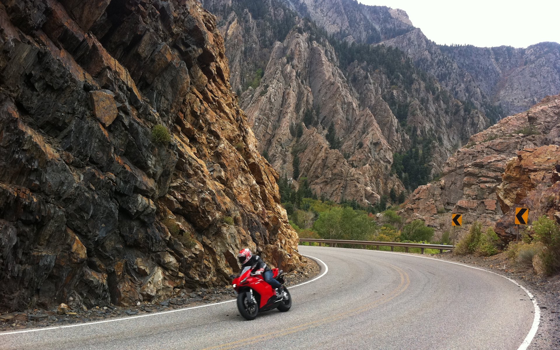 Red Ducati motorcycle leaning into a curve on a winding canyon road, framed by towering cliffs — HD PC desktop wallpaper background