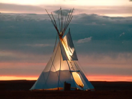 HD desktop wallpaper featuring a man-made tipi illuminated from within against a dramatic sunset sky.