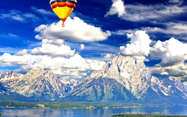 4K Ultra HD PC desktop wallpaper: a colorful hot air balloon vehicle floats over a tranquil lake with towering snow-capped mountains beneath dramatic cloud-filled skies.
