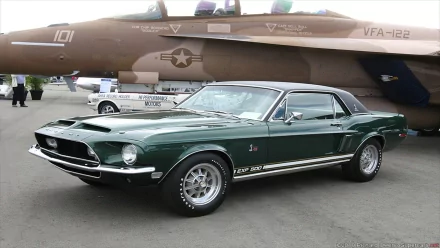 A classic green Ford Mustang parked in front of a military aircraft, showcasing its sleek design and vintage charm in this HD desktop wallpaper.