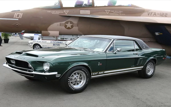 A classic green Ford Mustang parked in front of a military aircraft, showcasing its sleek design and vintage charm in this HD desktop wallpaper.