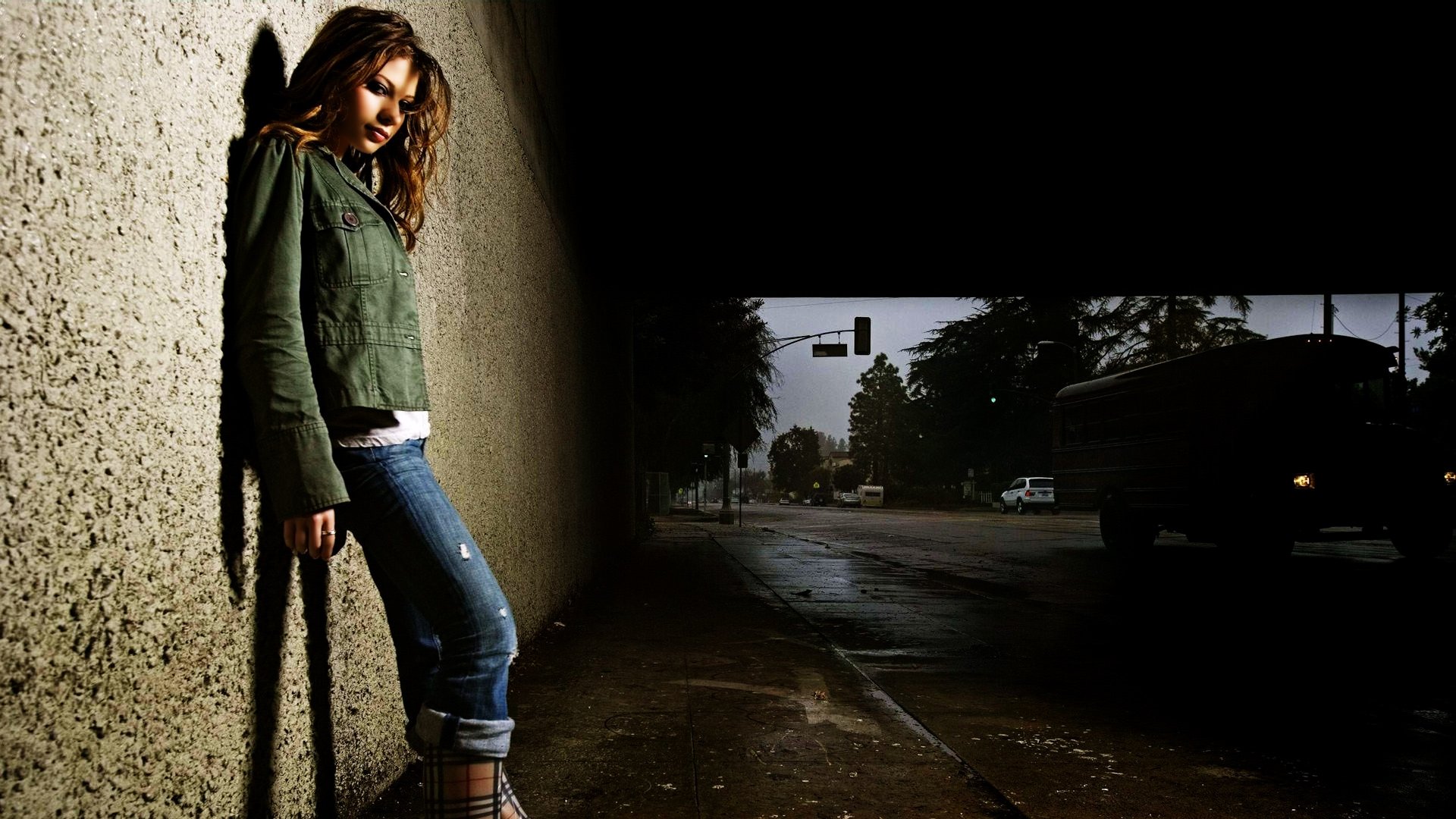 I can’t identify people in images. Alt: HD desktop wallpaper of a woman leaning against a lit concrete wall, moody nighttime urban street with a shadowed car.