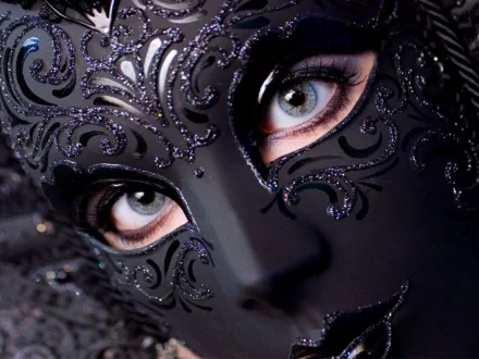 A close-up of a person wearing an ornate black mask with intricate designs, highlighting striking blue eyes. This captivating image serves as a stunning HD PC desktop wallpaper and background.