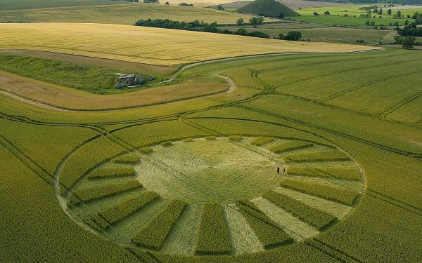 Aerial view of a man-made crop circle featuring intricate patterns, surrounded by lush fields and scenic countryside, presented as a stunning HD desktop wallpaper.