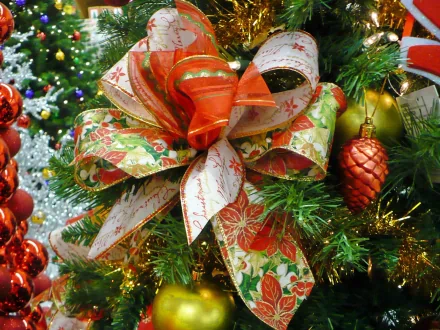A vibrant bow in red and gold adorns a Christmas tree, surrounded by colorful ornaments and festive decorations, creating a cheerful holiday atmosphere. HD wallpaper for a joyful Christmas theme.